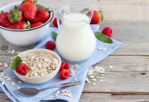 Rolled oats in a bowl with berries and milk on wood