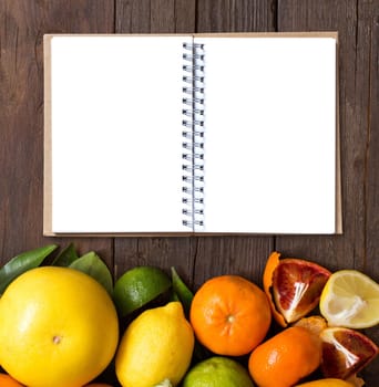 Fresh citrus fruits with notebook on wooden table