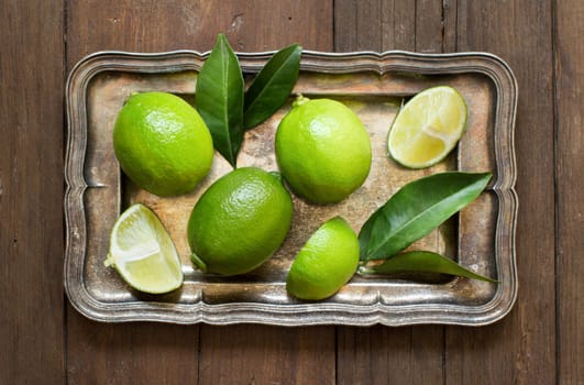 Fresh limes with leaves on a silver tray on a wooden table