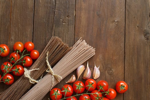 Two types of spaghetti, tomatoes and garlic on wood