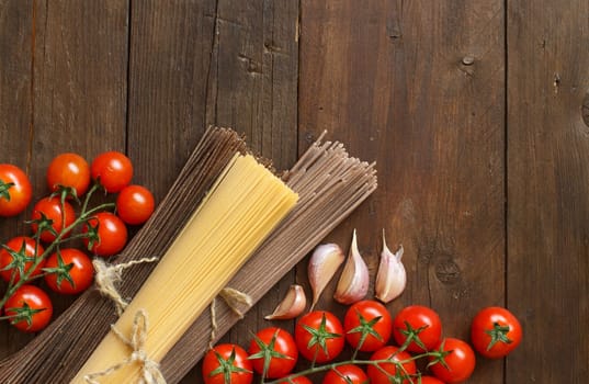 Three types of spaghetti, tomatoes and garlic on wood