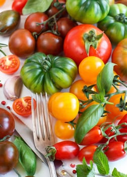 Colorful tomatoes, garlic, basil, fork and knife