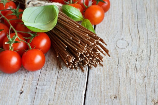 Wholegrain rye spaghetti, tomatoes and herbs on wood
