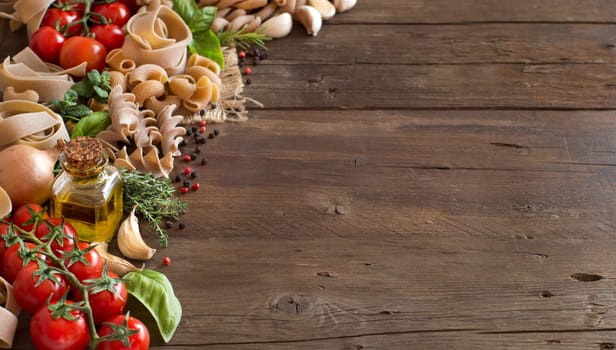 Whole wheat pasta, vegetables, herbs and olive oil on wooden background