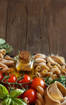 Whole wheat pasta, vegetables, herbs and olive oil on wooden background