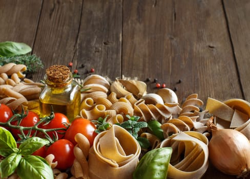 Whole wheat pasta, vegetables, herbs and olive oil on wooden background