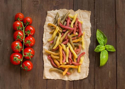 Tricolor pasta, vegetables, basil and cherry tomatoes on wooden background