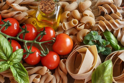 Whole wheat pasta, vegetables, herbs and olive oil on wooden background