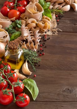 Whole wheat pasta, vegetables, herbs and olive oil on wood