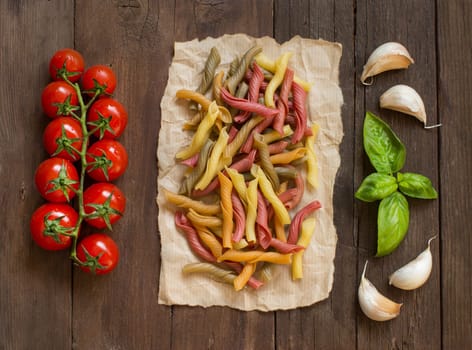 Tricolor pasta with cherry tomatoes, garlic and basil on wooden background