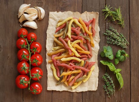 Colorful pasta, vegetables and herbs on wooden background