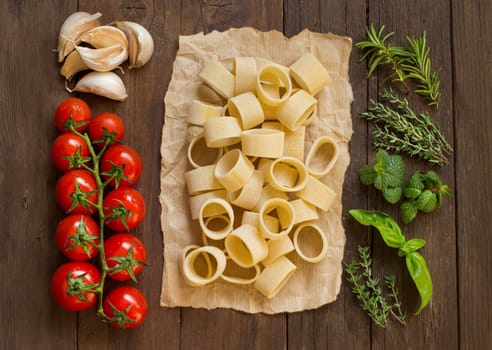 Italian pasta, vegetables, herbs and olive oil on wooden background