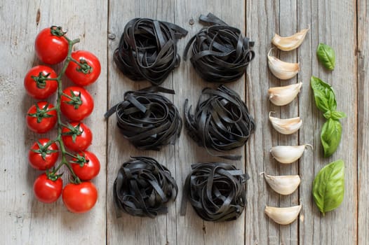 Dry Black Tagliatelle pasta with cherry tomatoes, garlic and basil on wood