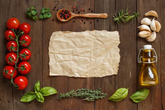 Craft paper with border of vegetables, herbs and olive oil on wooden background