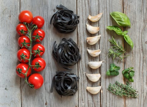 Dry Black Tagliatelle pasta with cherry tomatoes, garlic and herbs on wood