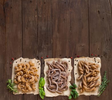 Whole wheat pasta and herbs on a wooden background