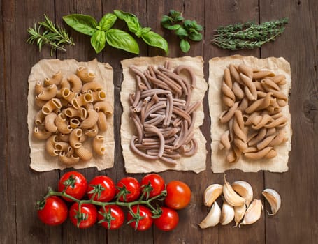 Whole wheat pasta, vegetables, herbs and olive oil on wooden background