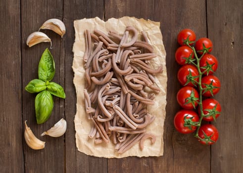 Whole spelt pasta, tomatoes, garlic and basil on wooden background