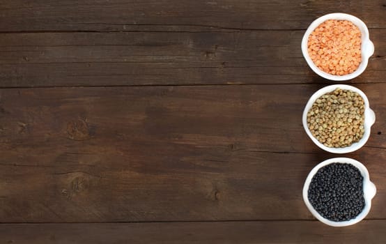 Red, green and black lentis in bowls on wooden background