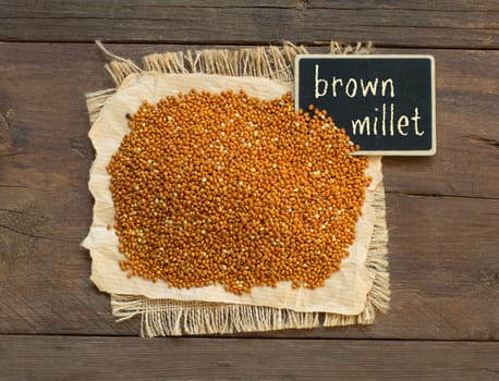 Whole brown millet pile with a small chalkboard top view