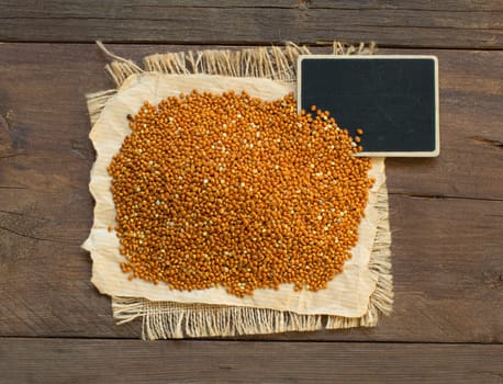Whole brown millet pile with a small chalkboard top view