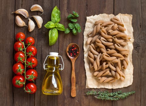 Whole wheat pasta, vegetables, herbs and olive oil on wooden background