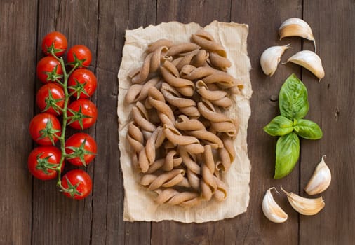 Whole wheat pasta, tomatoes and basil on wooden background