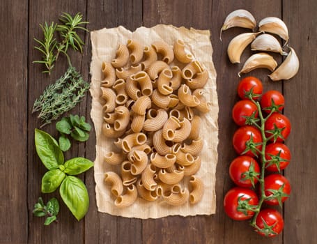 Whole wheat pasta, vegetables, herbs and olive oil on wooden background