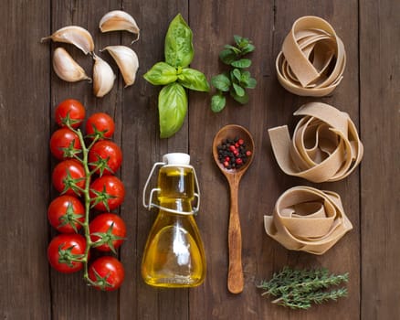 Whole wheat pasta, vegetables, herbs and olive oil on wooden background