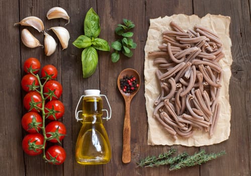Whole wheat pasta, vegetables, herbs and olive oil on wooden background