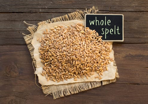 Whole unpolished spelt in a with a small chalkboard on wooden table