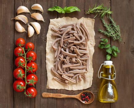 Whole spelt pasta, vegetables, herbs and olive oil on wooden background
