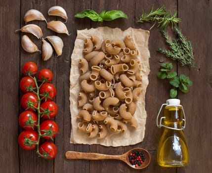 Whole wheat pasta, vegetables, herbs and olive oil on wooden background