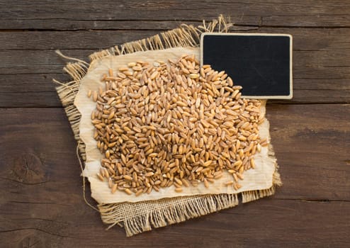 Whole unpolished spelt in a with a small chalkboard on wooden table