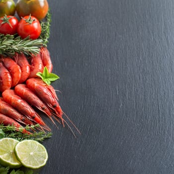 Raw shrimps with tomatoes, lime and herbs over dark background
