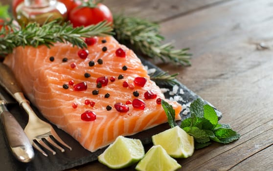 Salmon with vegetables and herbs on wooden background