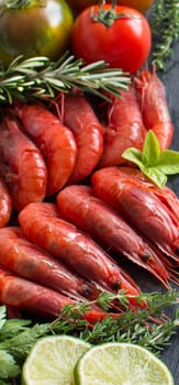 Raw shrimps with tomatoes, lime and herbs over dark background