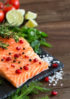 Salmon with vegetables and herbs on wooden background
