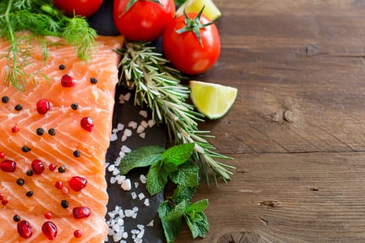 Salmon with vegetables and herbs on wooden background