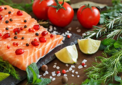 Salmon with vegetables and herbs on wooden background