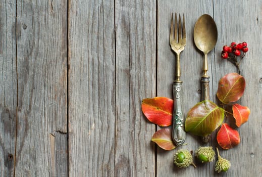 Vintage fork and knife with fall leaves, acorns and berries on the old wooden table