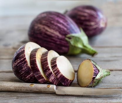 Fresh Raw striped eggplants and slices with knife on old wooden table