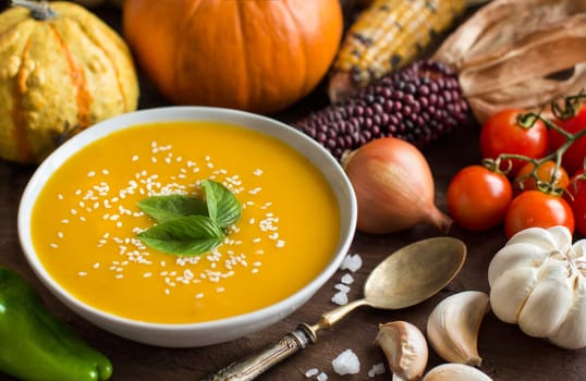 Fresh pumpkin soup with a spoon and vegetables on a wooden table