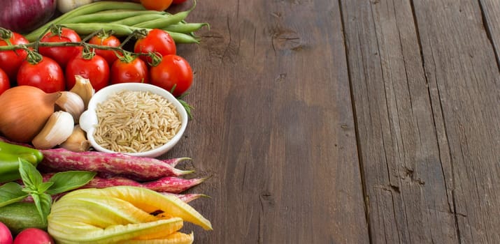Unpolished raw rice and vegetables on a wooden background