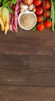 Unpolished raw rice and vegetables on a wooden background