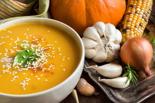 Fresh pumpkin soup with a spoon and vegetables on a wooden table