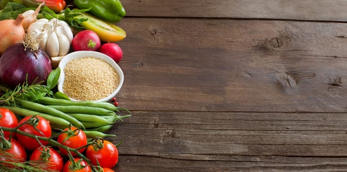 CousCous in a bowl and fresh vegetables on wood