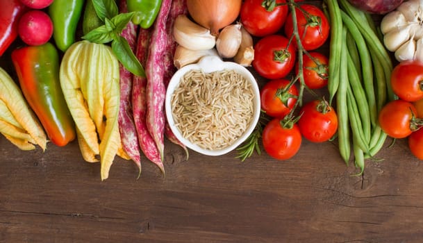 Unpolished raw rice and vegetables on a wooden background