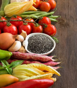 Raw chia seeds in bowl and vegetables on a wooden table