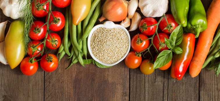Quinoa in a bowl and fresh vegetables on a wooden table